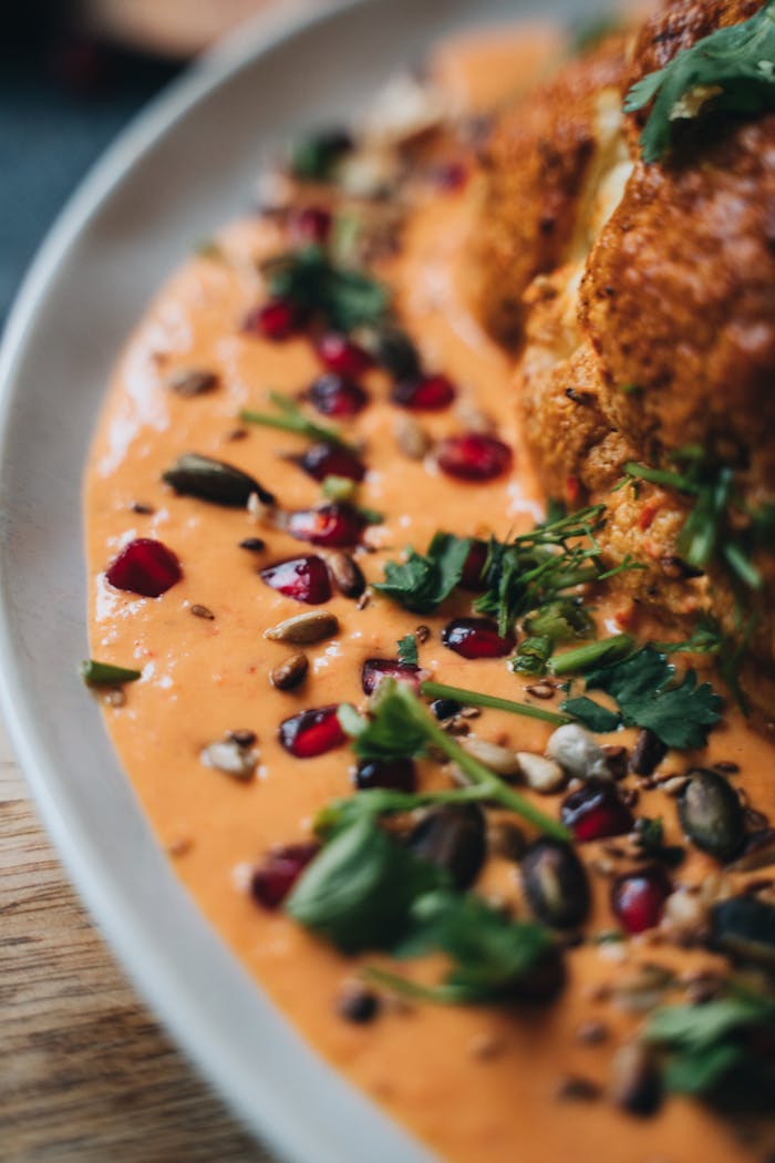 Close-up of roasted cauliflower served with a vibrant spiced sauce, garnished with seeds and herbs.