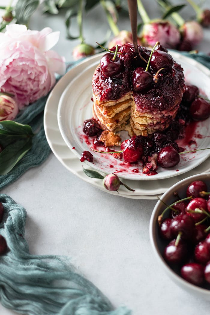 Delicious cherry-topped pancakes styled with peonies for a rustic brunch setting.